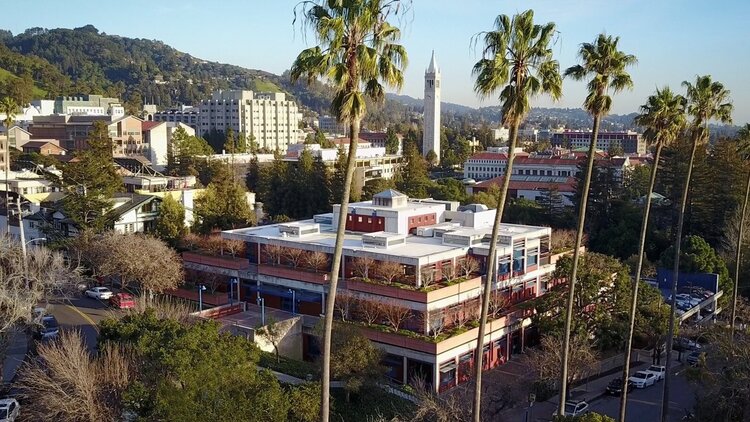 Top angle photo of a Graduate Theological Union building on a sunny day, with palm trees in front of the building.